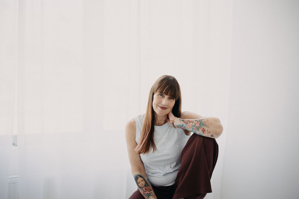 Katrin Seelenbalm sitzt entspannt am Boden, lächelt sanft und blickt ruhig in die Kamera.