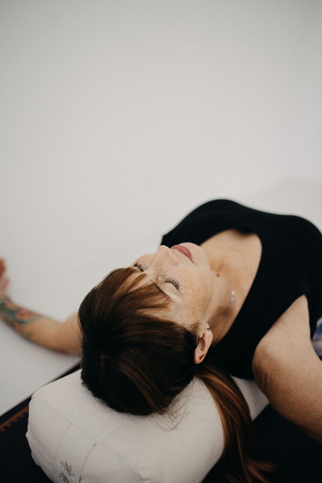 Frau in Rückenlage auf Bolster, Augen geschlossen – Yin Yoga, achtsame Gruppenstunde bei Seelenbalm. Mindful Hatha Yoga Seelenbalm